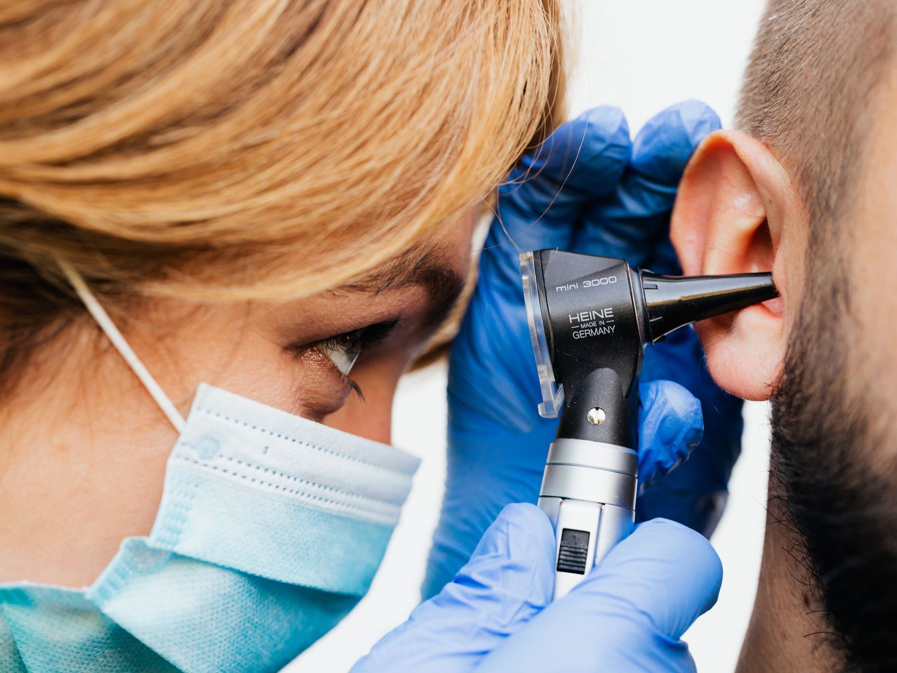 Close-up of a gloved hand using an otoscope to examine a patient's ear