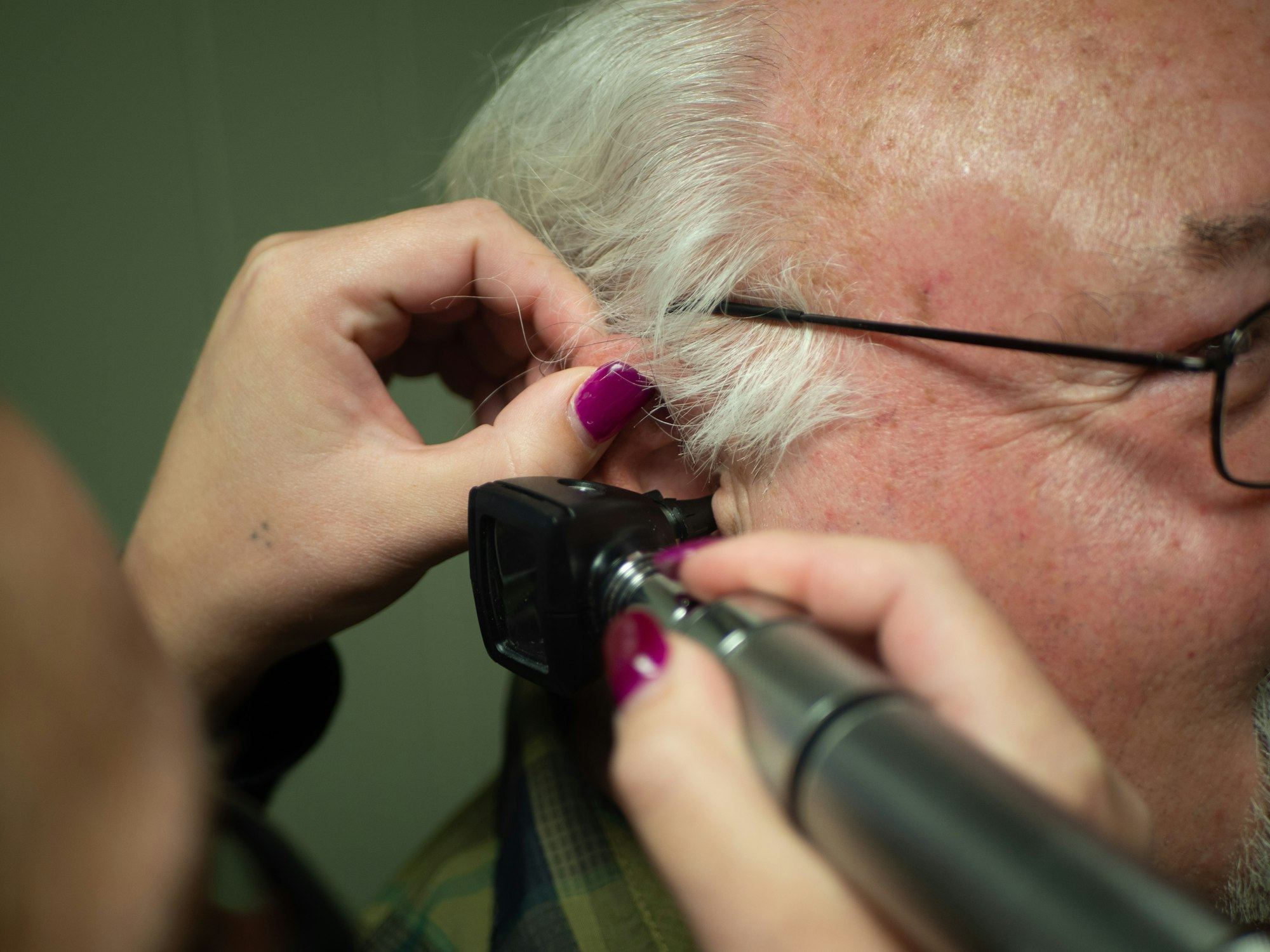 A clinician's gloved hands inserting a probe into an older man's ear
