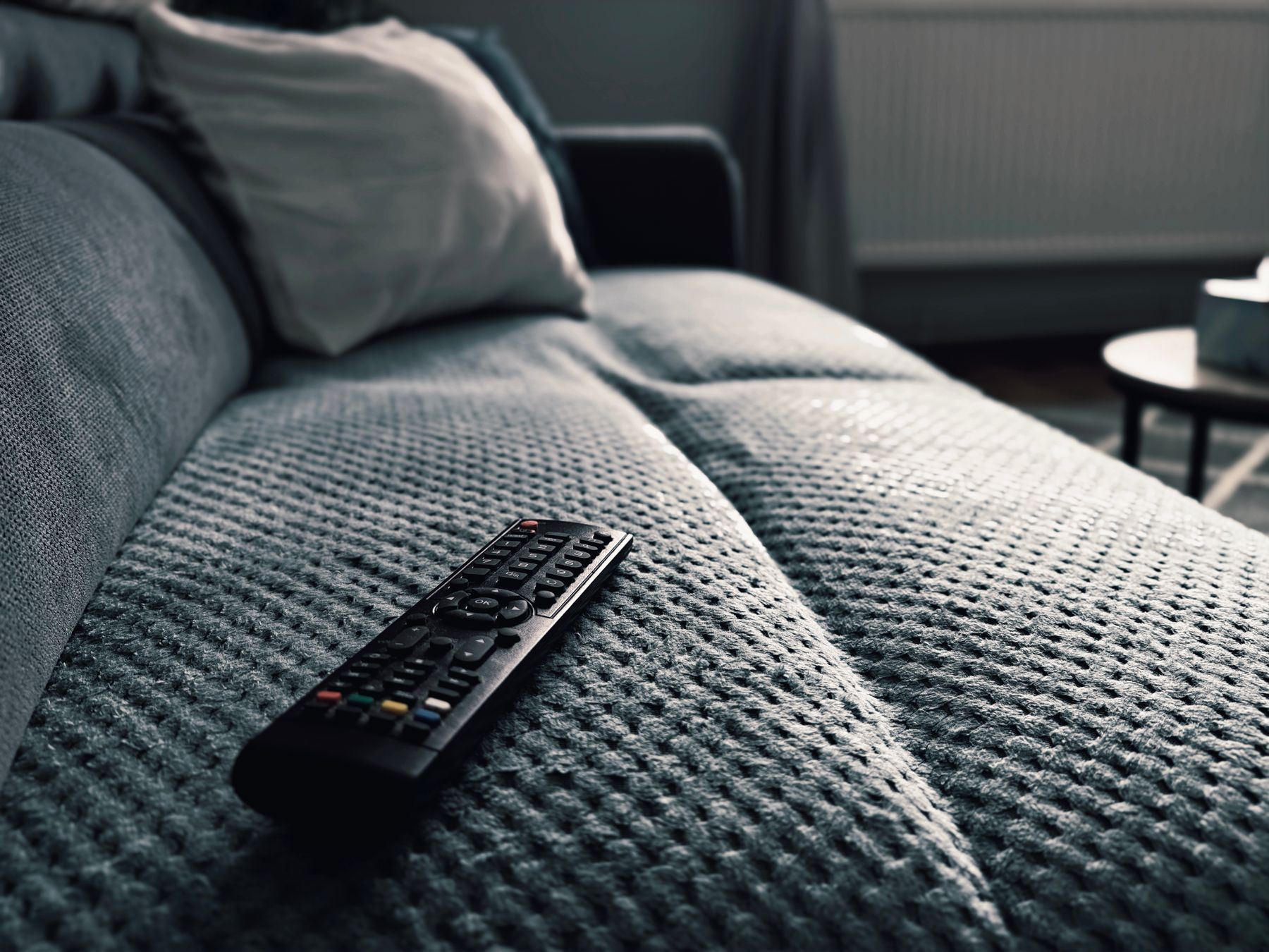 A TV remote control resting on the arm of a grey sofa.