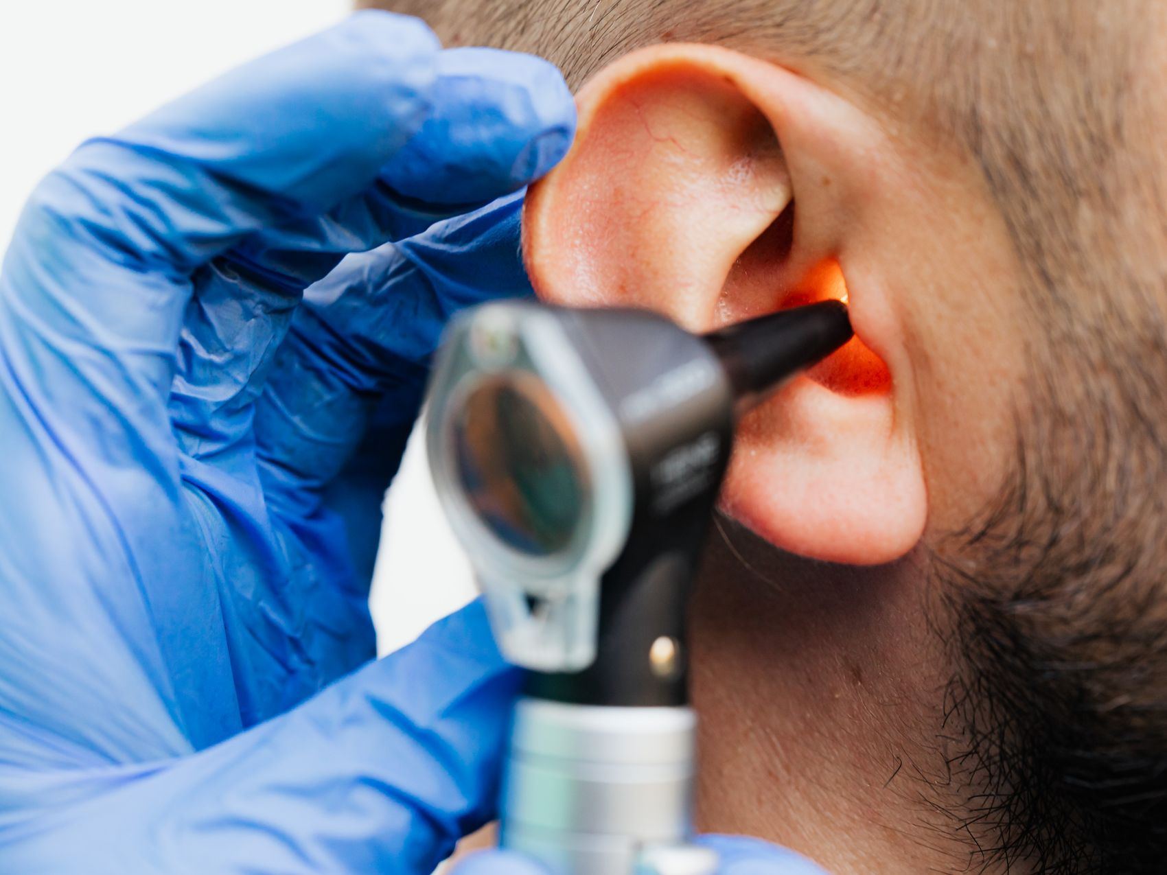 A gloved hand uses an otoscope to examine the inside of a person's ear.