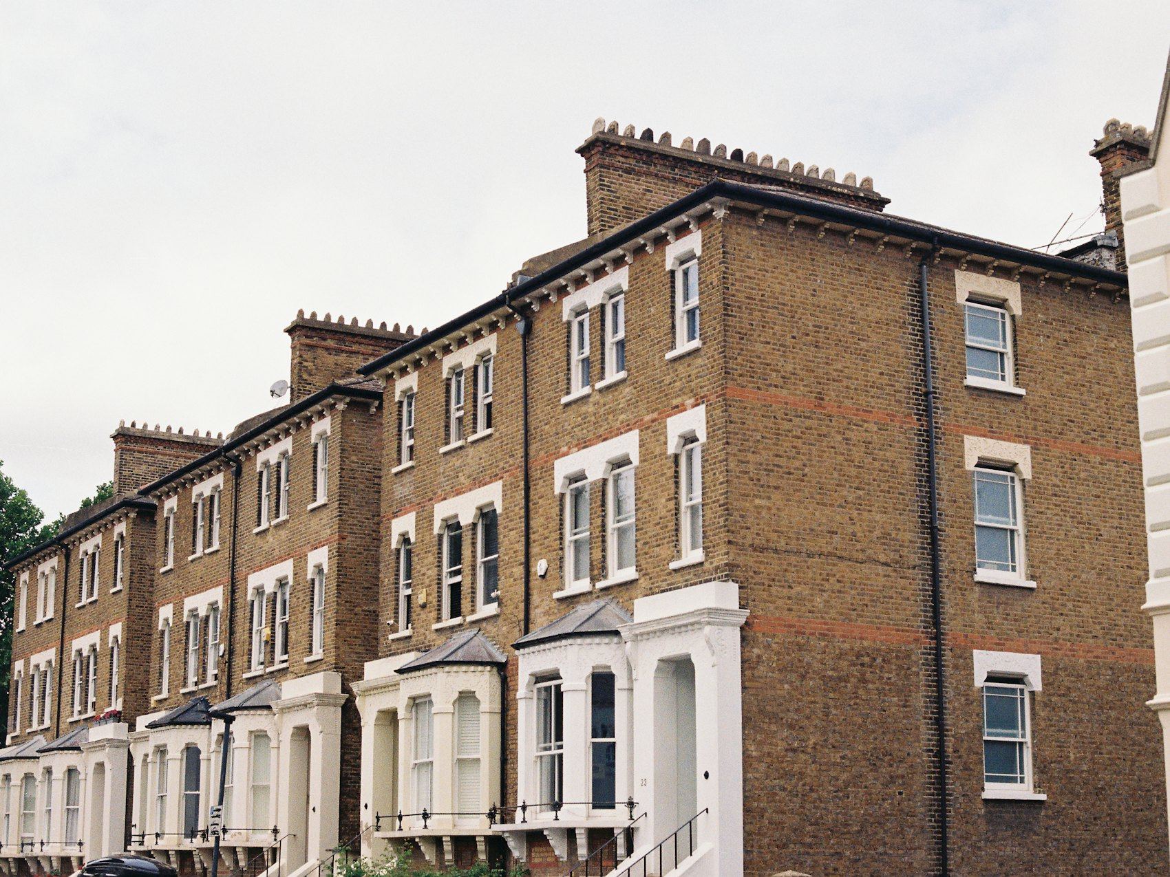 A row of Victorian terraced brick houses with bay windows under an overcast sky.
